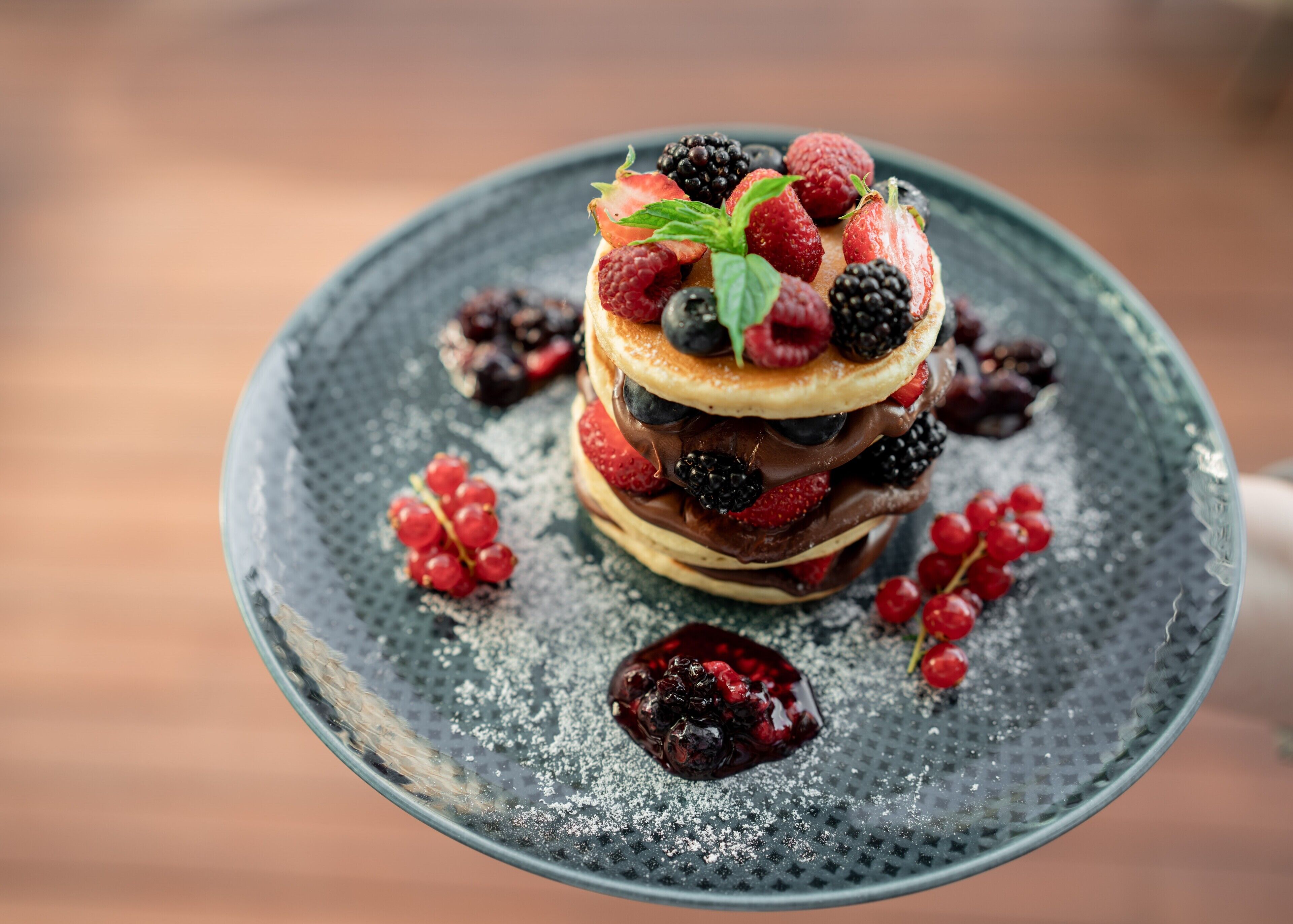 A dessert with multiple layers of pancakes, berries, and chocolate, served on a textured plate.