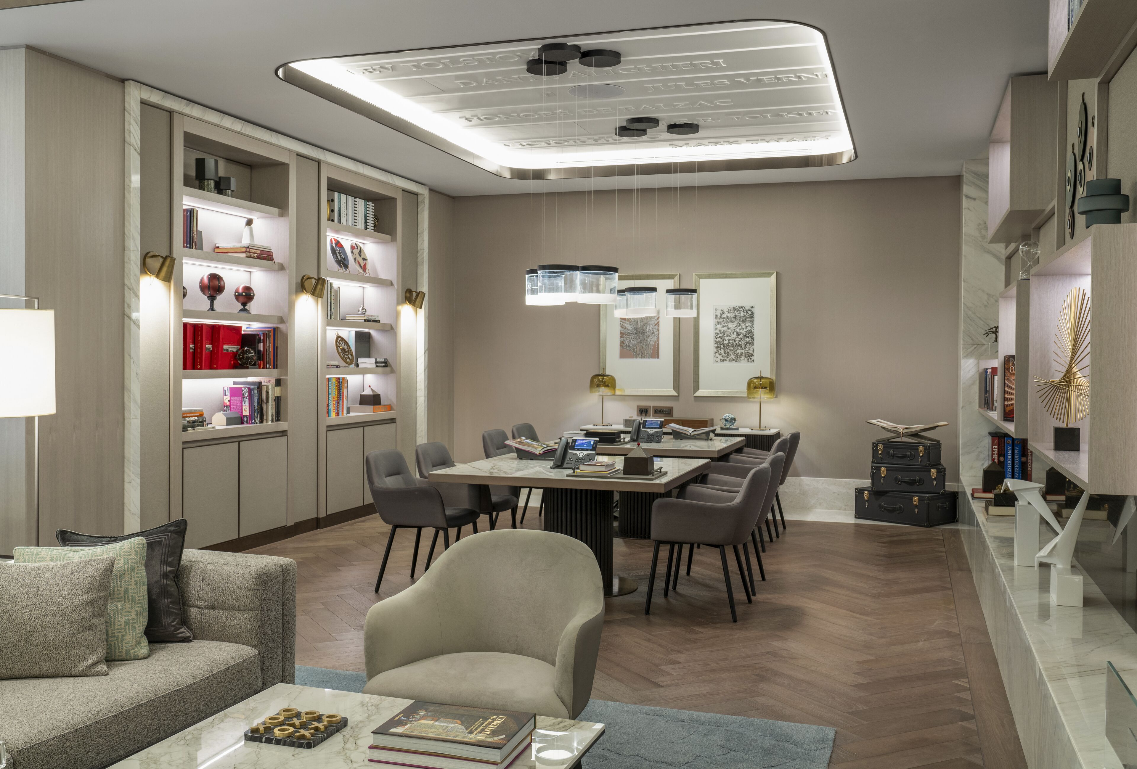 A modern, well-lit living room with a dining area, featuring a large table, comfortable seating, and built-in shelving with books and decorative items.