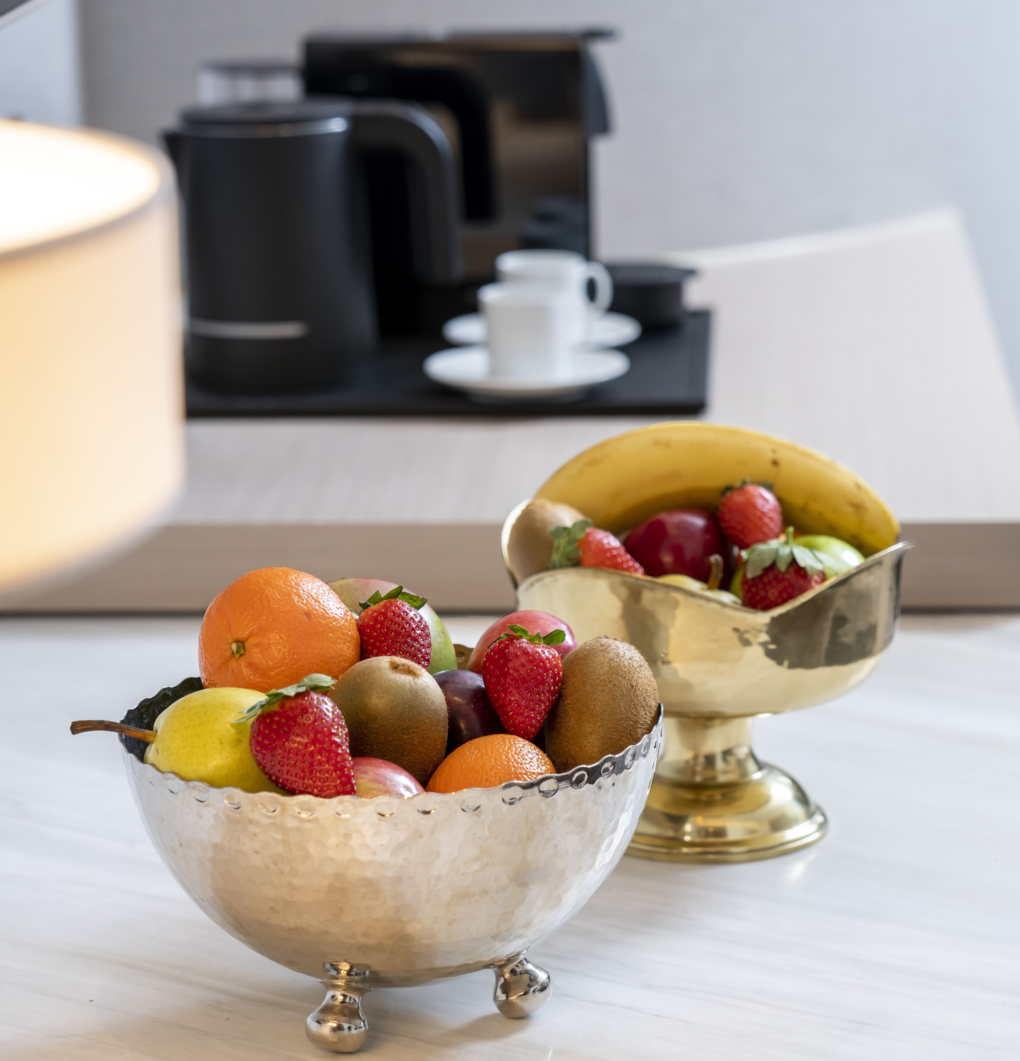 Two metallic bowls filled with fruits on a table.