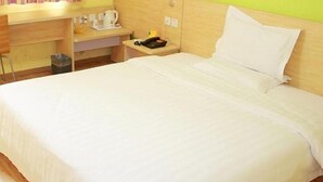 Een hotelkamer met een bed, nachtkastje met lamp, klein bureau met koffiezetapparaat en een prullenbak.