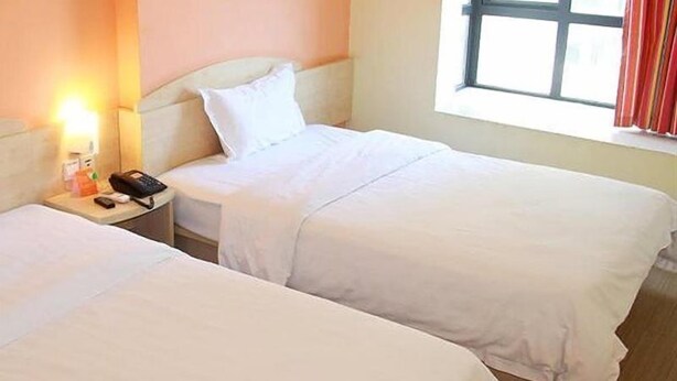 Een hotelkamer met twee eenpersoonsbedden, een nachtkastje met telefoon en lamp, en een raam met gordijnen.