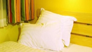 Een bed met witte lakens in een kamer met gele wanden en een gestreept gordijn.