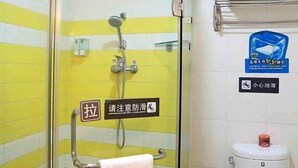 Een badkamer met een wand betegeld in geel en wit, een glazen douchecabine, een toilet en een handdoekhouder.