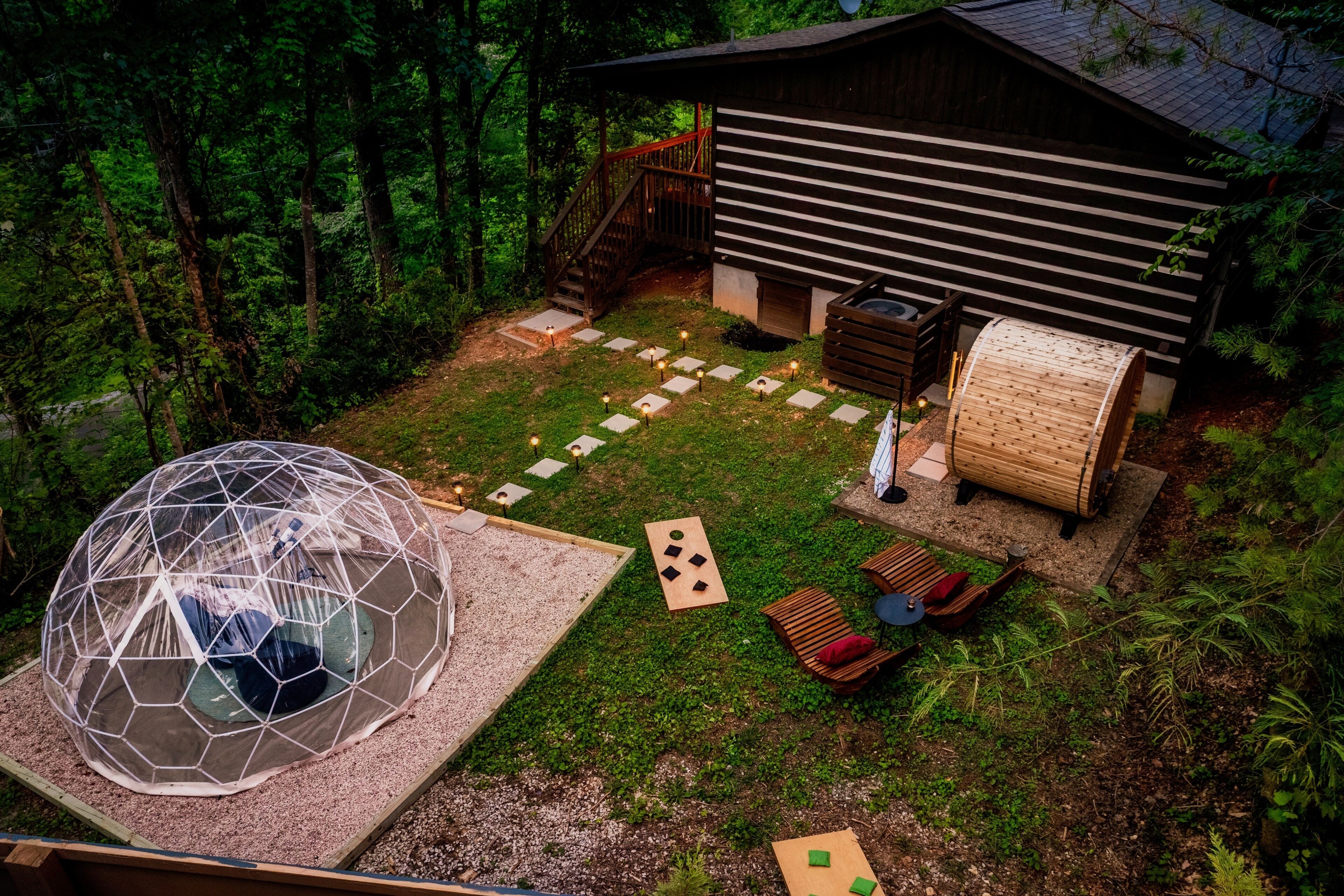 Une structure en forme de dôme géodésique, un chalet en bois et une terrasse avec des sièges d’extérieur.