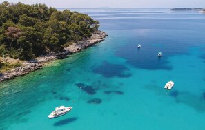 Vue aérienne d’une zone côtière avec des eaux turquoise limpides, un littoral rocheux et une végétation luxuriante.