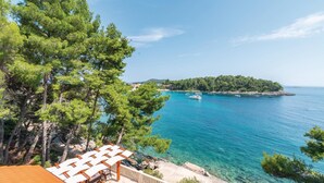 A coastal view with clear turquoise waters, a small island in the distance, and a wooden deck with white umbrellas. - Awesome Home in Prizba With Wifi and 3 Bedrooms (Blato)