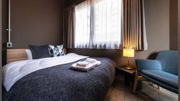 A hotel room with a large bed, a bedside table with a lamp, a chair, and a window with curtains.