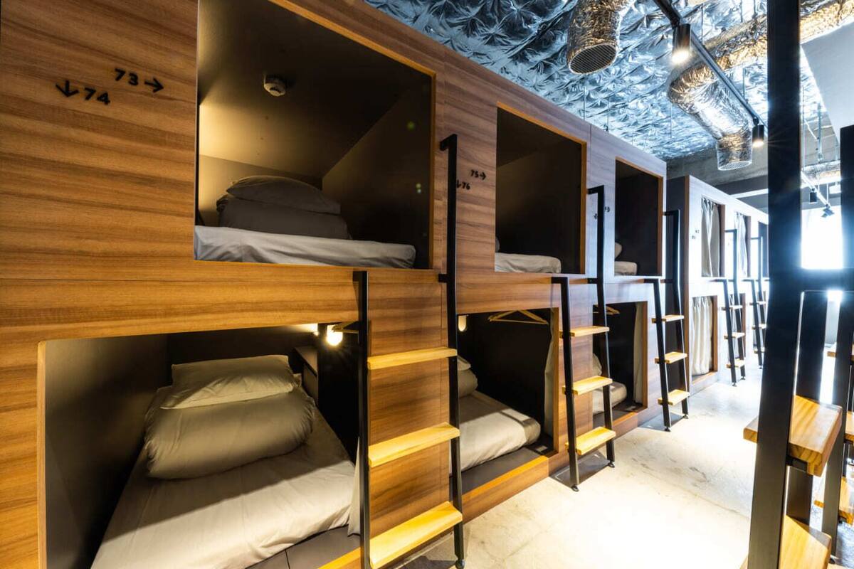 Habitación de hostal con literas, paredes de madera y techo con conductos a la vista.