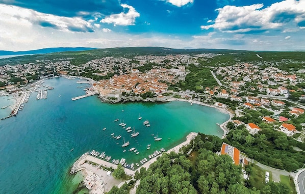An aerial view of a coastal town with a marina, buildings, and surrounding greenery.
