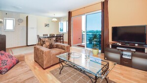 Un salon moderne avec un canapé, une table basse en verre, un téléviseur à écran plat et un balcon offrant une vue agréable.