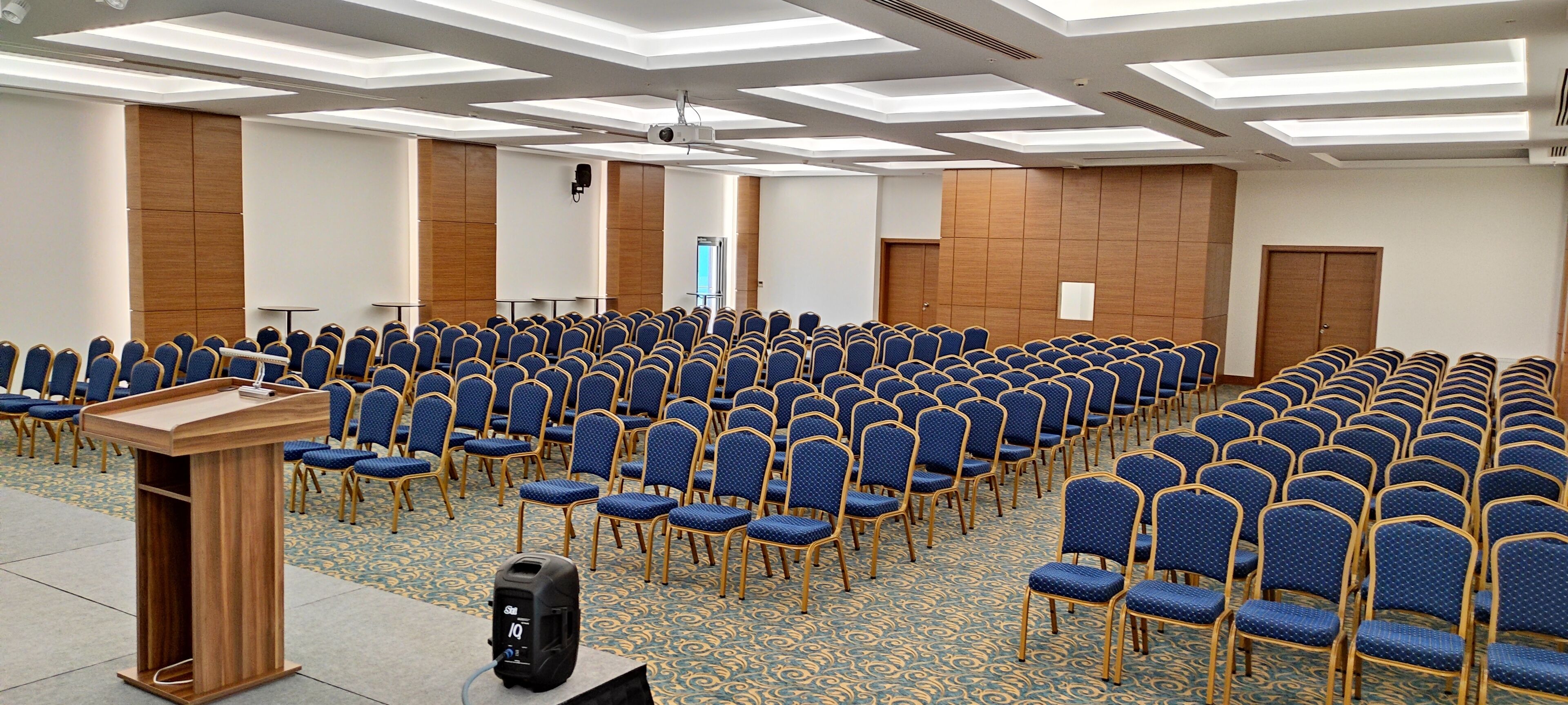 A conference room with rows of blue chairs, a wooden podium, and a projector screen.