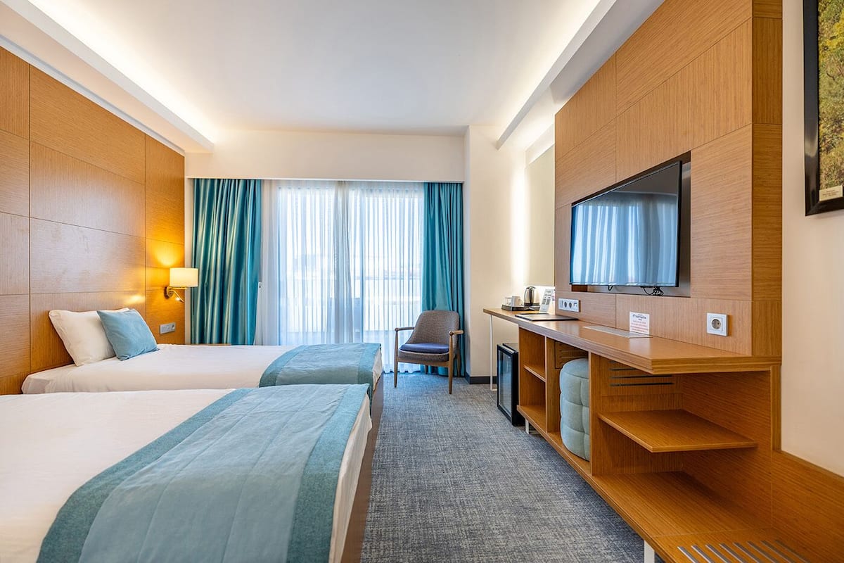 Habitación de hotel con dos camas, un escritorio, un televisor, una silla y una ventana con cortinas.