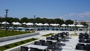 Zona de piscina con varias tumbonas, sombrillas y mesas de comedor.