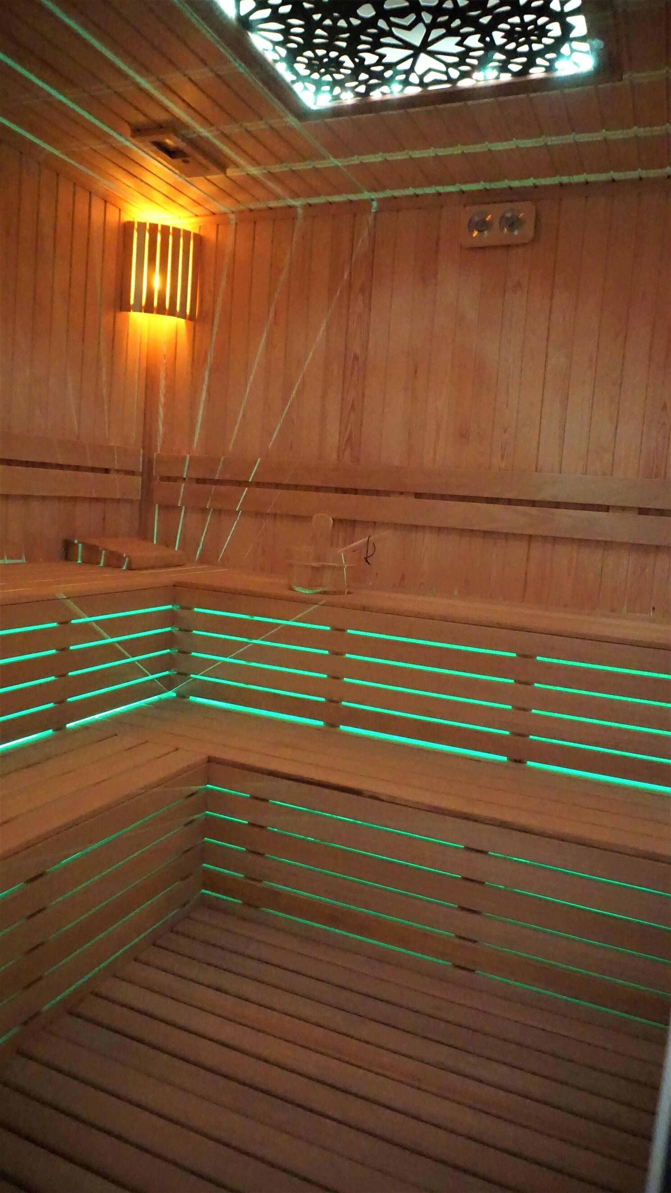 A sauna with wooden walls and benches, featuring green LED lighting along the benches.