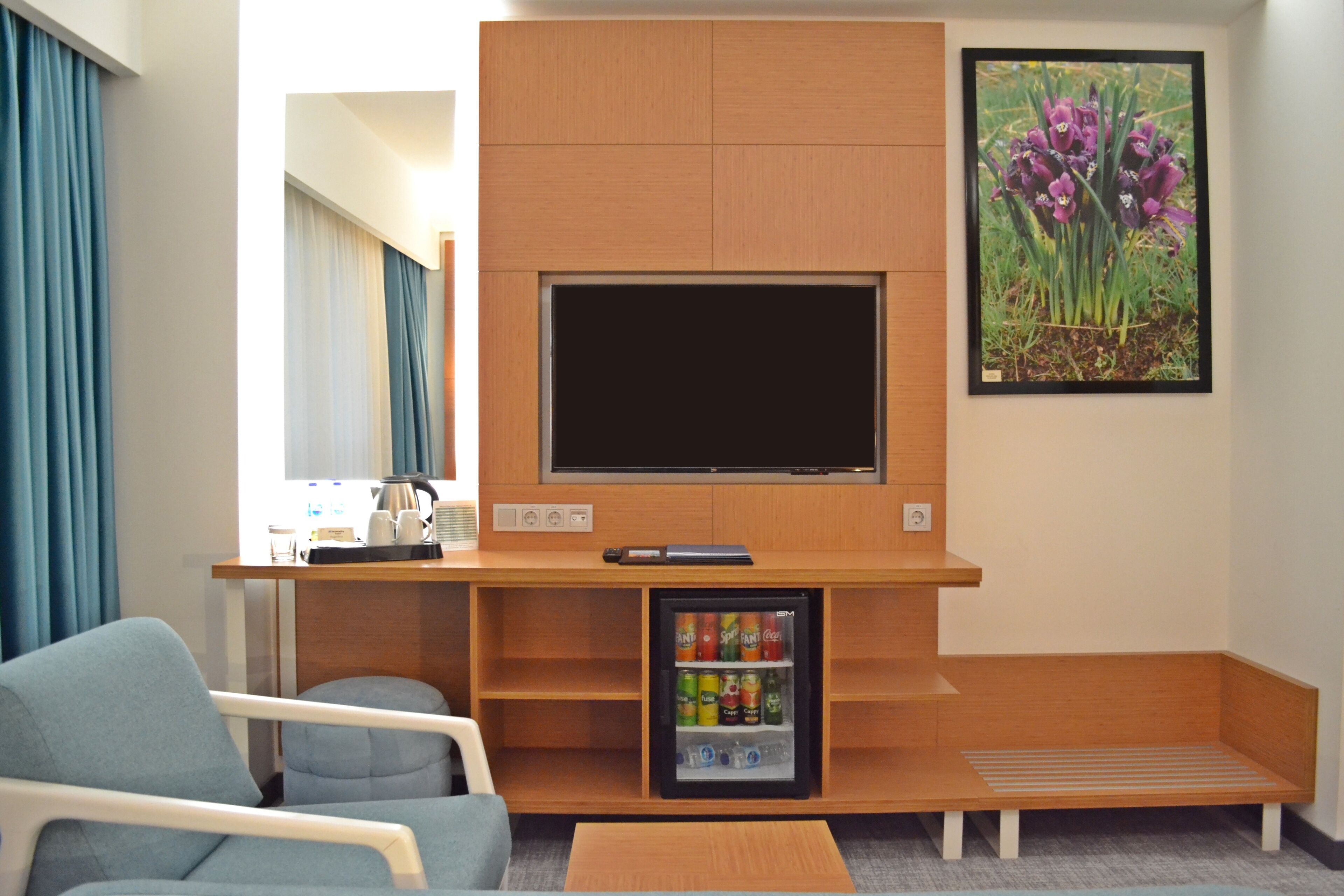 A hotel room with a TV, seating area, and a mini-fridge with beverages.