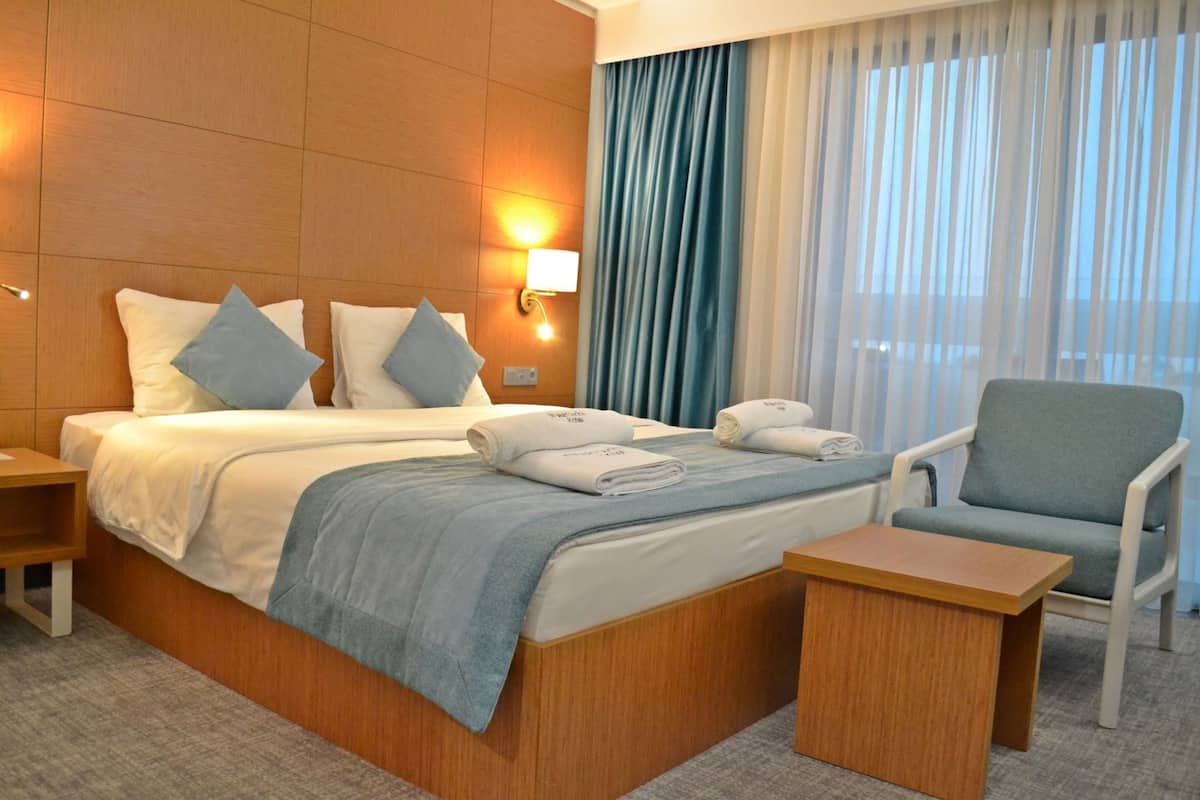 Una habitación de hotel con una cama grande, dos mesitas de noche, una silla y un ventanal con cortinas.