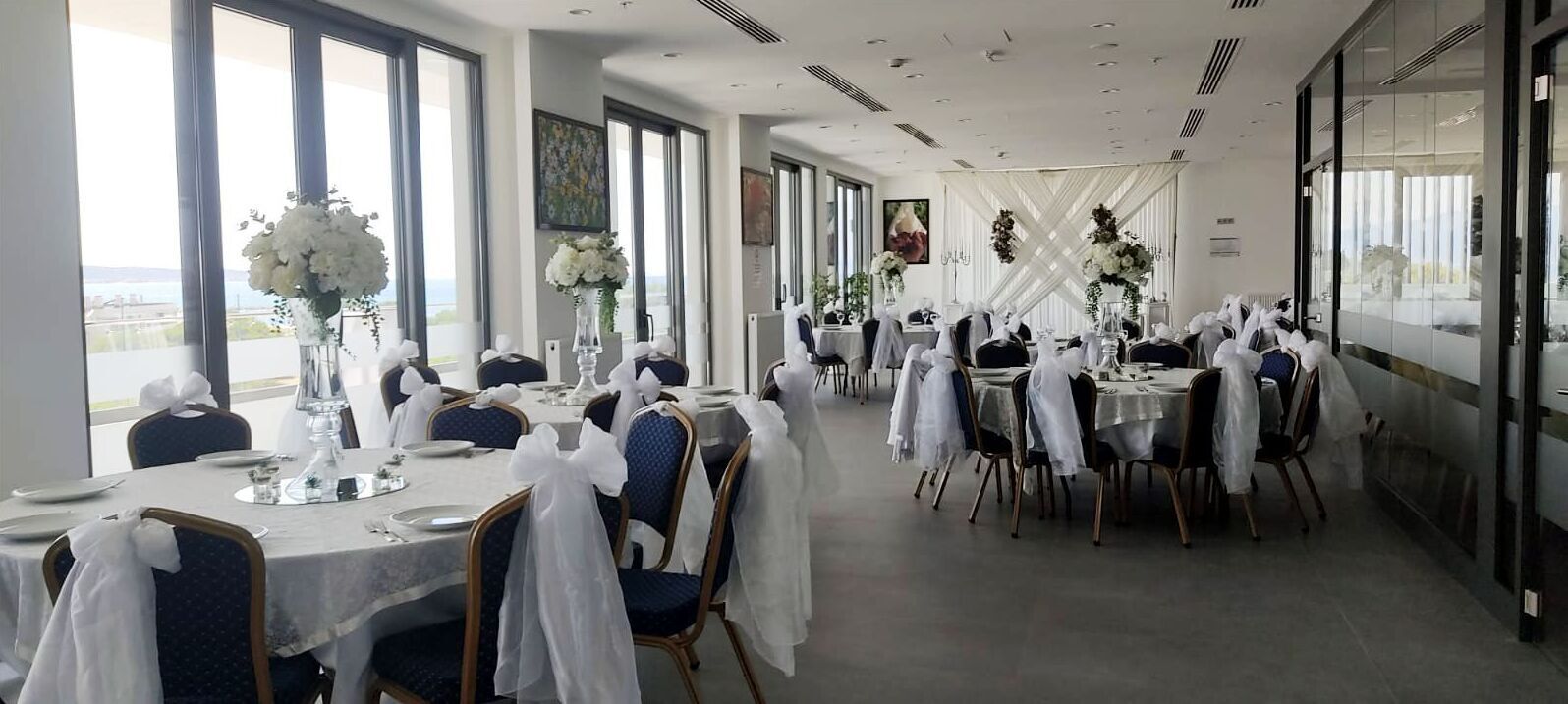 Une salle de banquet avec des tables rondes, des nappes blanches et des chaises ornées de rubans blancs.
