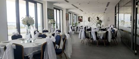 Une salle de banquet avec des tables rondes, des nappes blanches et des chaises ornées de rubans blancs.