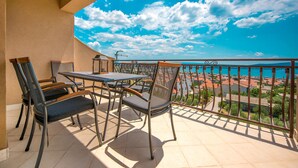 Ein Balkon mit Tisch und Stühlen, der Blick auf die Küste mit Gebäuden und einem klaren Himmel bietet.
