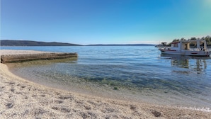 Ein sauberer Strand mit ruhigem Wasser, ein Boot an der rechten Seite und eine entfernte Küstenlinie.