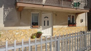 Un bâtiment doté d’une façade en pierre, d’une porte blanche et de deux fenêtres ornées de jardinières.