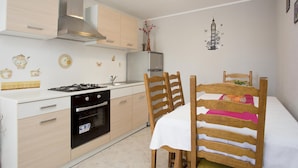 Une cuisine compacte équipée d’une cuisinière à gaz, d’un four et d’une hotte aspirante moderne en acier inoxydable. On y trouve une table à manger avec des chaises en bois et une nappe blanche.