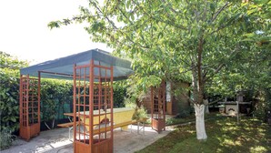 Un espace extérieur abrité, avec un banc en bois et une table, entouré de verdure et d’un arbre.