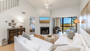 Un salón amplio con chimenea, sofás blancos, una mesa de centro y un ventanal con vistas al exterior.
