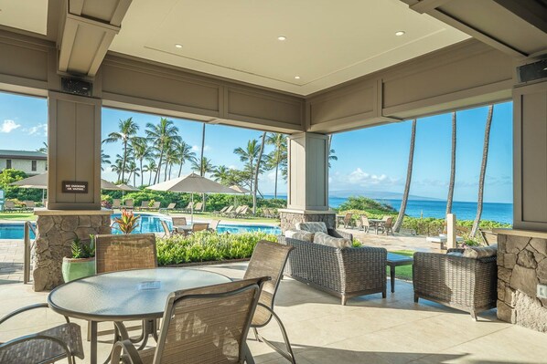 A covered outdoor area with a pool, lounge chairs, and a view of the ocean.