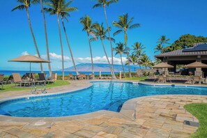 A swimming pool with lounge chairs and umbrellas, surrounded by palm trees and a view of a mountain.