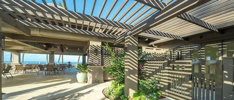 Uma área de pátio externa com estrutura de pérgola, assentos e plantas em vasos.