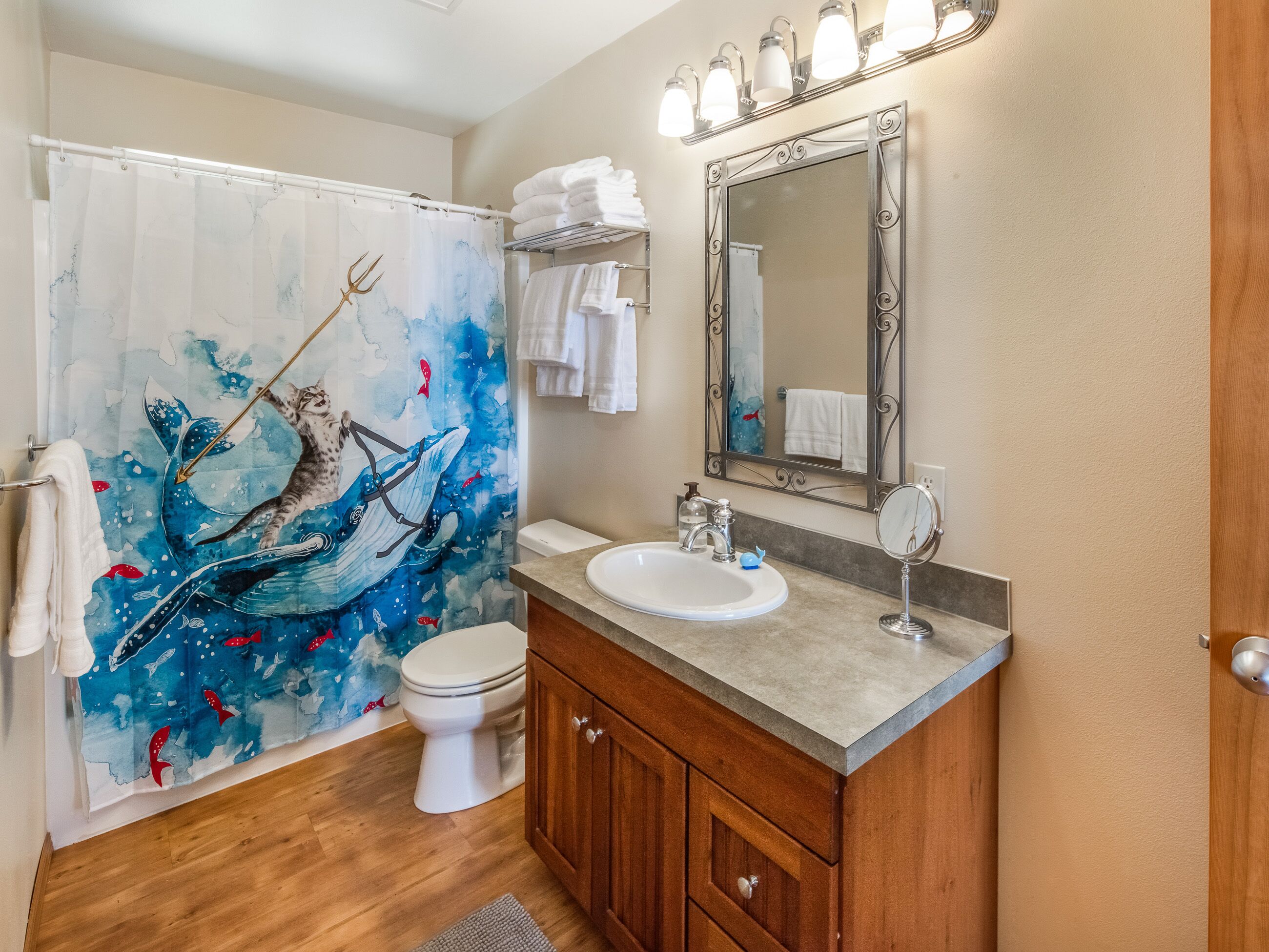 Un baño con cortina de ducha que muestra una ballena y peces, un inodoro blanco, un tocador con espejo y un lavabo.