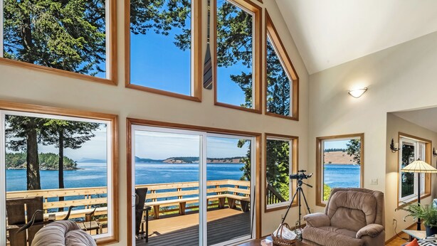 A spacious living room with large windows offering a view of the sea and a deck area with a wooden bench. - Waterfront w/ Seasonal Dock! (Rendezvous Retreat) (Friday Harbor)