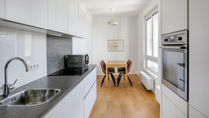 A modern kitchen with white cabinets, a black countertop, a built-in oven, and a dining area with a table and chairs. - Modern Landstraße 1BR, walk to Metro U1 and Hauptbahnhof, by Blueground (Vienna)
