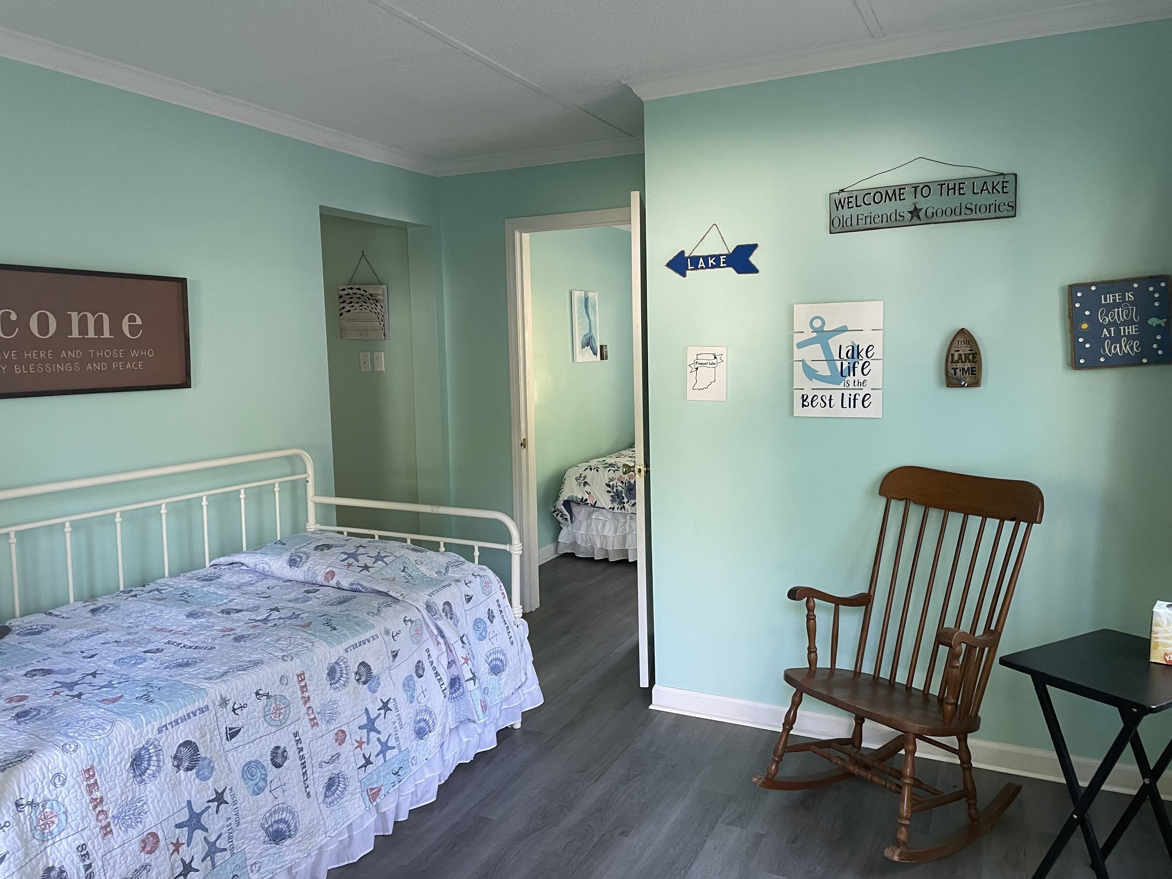 A bedroom with a bed, a rocking chair, and a wall with various signs and decorations.