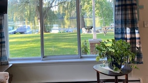 A room with a large window overlooking a grassy area and a body of water. There is a small table with a potted plant on it. - Romantic House on the Lake-Hot Tub Pet Friendly-kayaks-Fishing Boat. Sleeps 8 (Pleasant Lake)