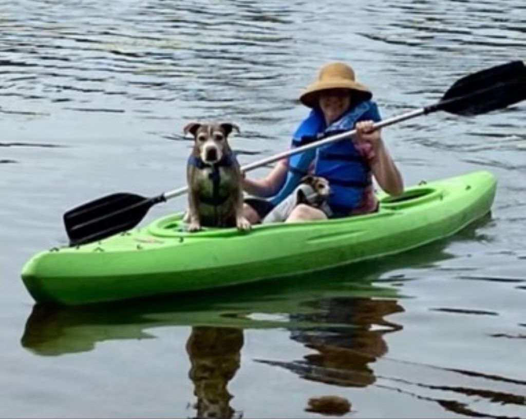 Uma pessoa num caiaque com dois cães, um de cada lado.