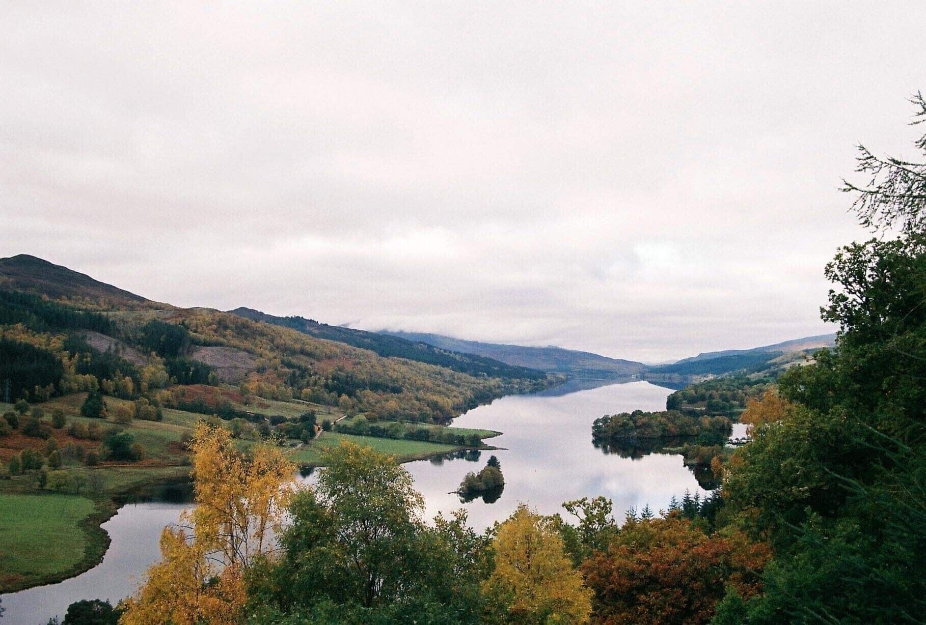 A serene landscape with a lake surrounded by hills and autumn foliage.