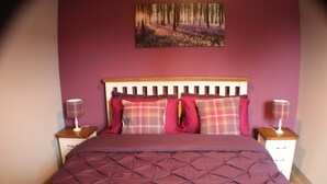 A neatly made bed with a patterned bedspread and multiple pillows, two bedside lamps, and a painting on the wall. - 1 Bed Flat - Sleeps 2 - Wifi (Pitlochry)