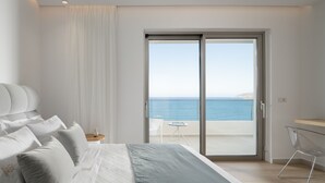 A bedroom with a bed, white curtains, a small table with a vase, and a view of the sea through a sliding door. - Ode Iconic Residence, forever in blue - Best Villa (Bali)