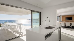 A modern kitchen with a large island, a dining area with white chairs, and a view of the sea. - Ode Iconic Residence, forever in blue - Best Villa (Bali)