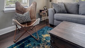Een woonkamer met een schommelstoel, een bank, een salontafel, een lamp en een vloerkleed.
