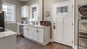 Una cocina con armarios blancos, un microondas y una puerta con ventanal.