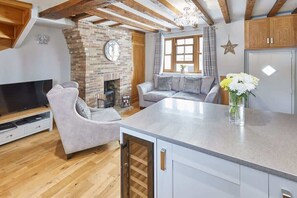 A modern living room with a fireplace, a sofa, a TV, and a kitchen area with a countertop and cabinets.