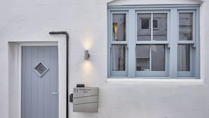 Un bâtiment blanc avec une porte grise et une fenêtre dont les bords sont bleus.