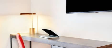 A modern desk with a laptop, a red chair, and a wall-mounted TV.
