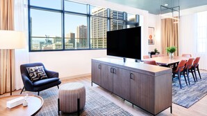 A modern living room with a large TV, a dining area, and a view of the city skyline through large windows. - Hyatt Centric Downtown Denver (Denver)