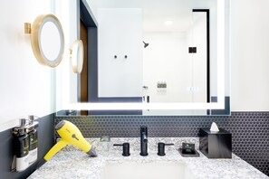 Un baño con un espejo grande, un lavamanos, un secador de pelo y artículos de aseo.