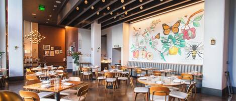 A restaurant with multiple tables and chairs, a large mural on the wall, and a ceiling with recessed lighting.