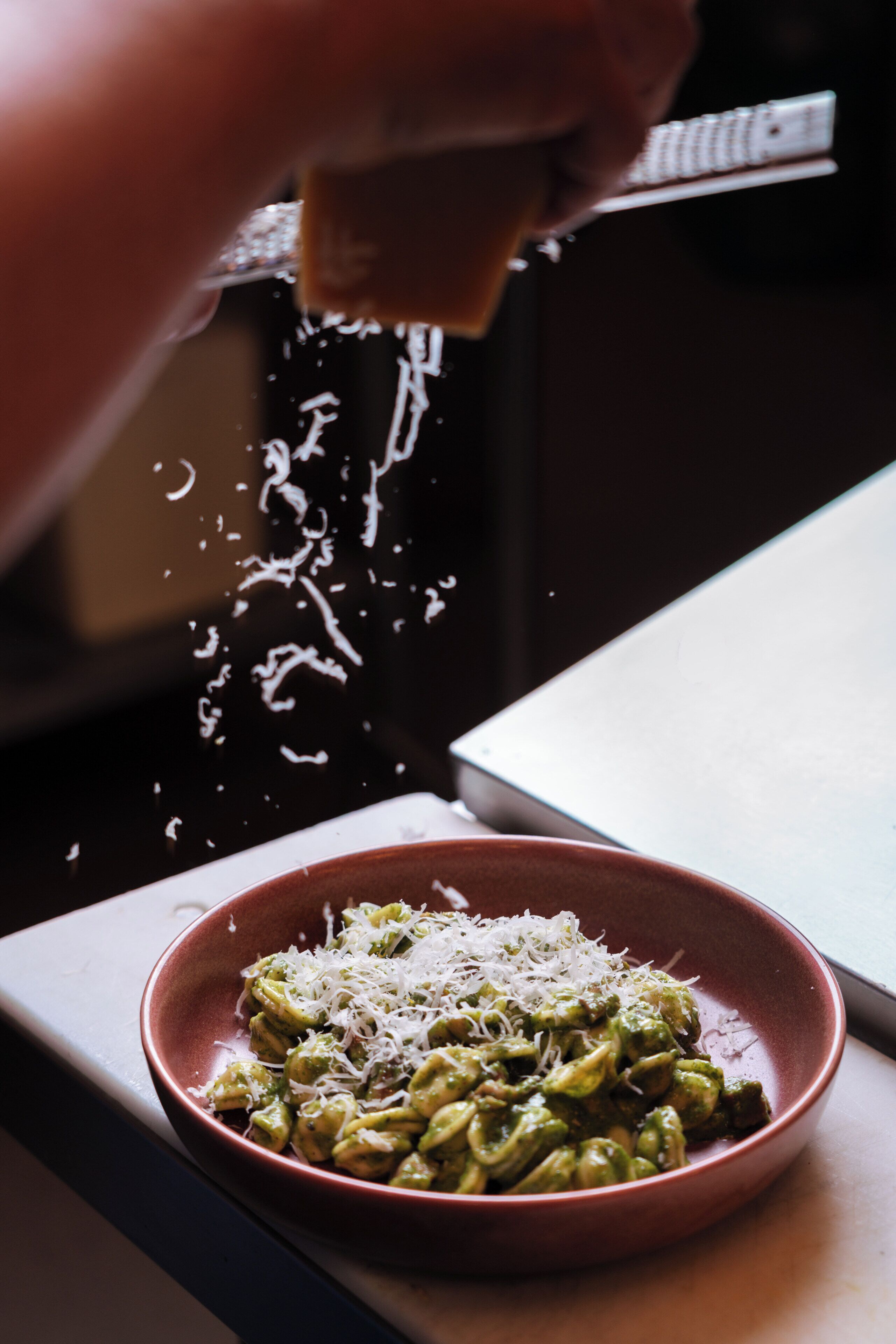 A bowl of pasta with grated cheese being sprinkled on it.